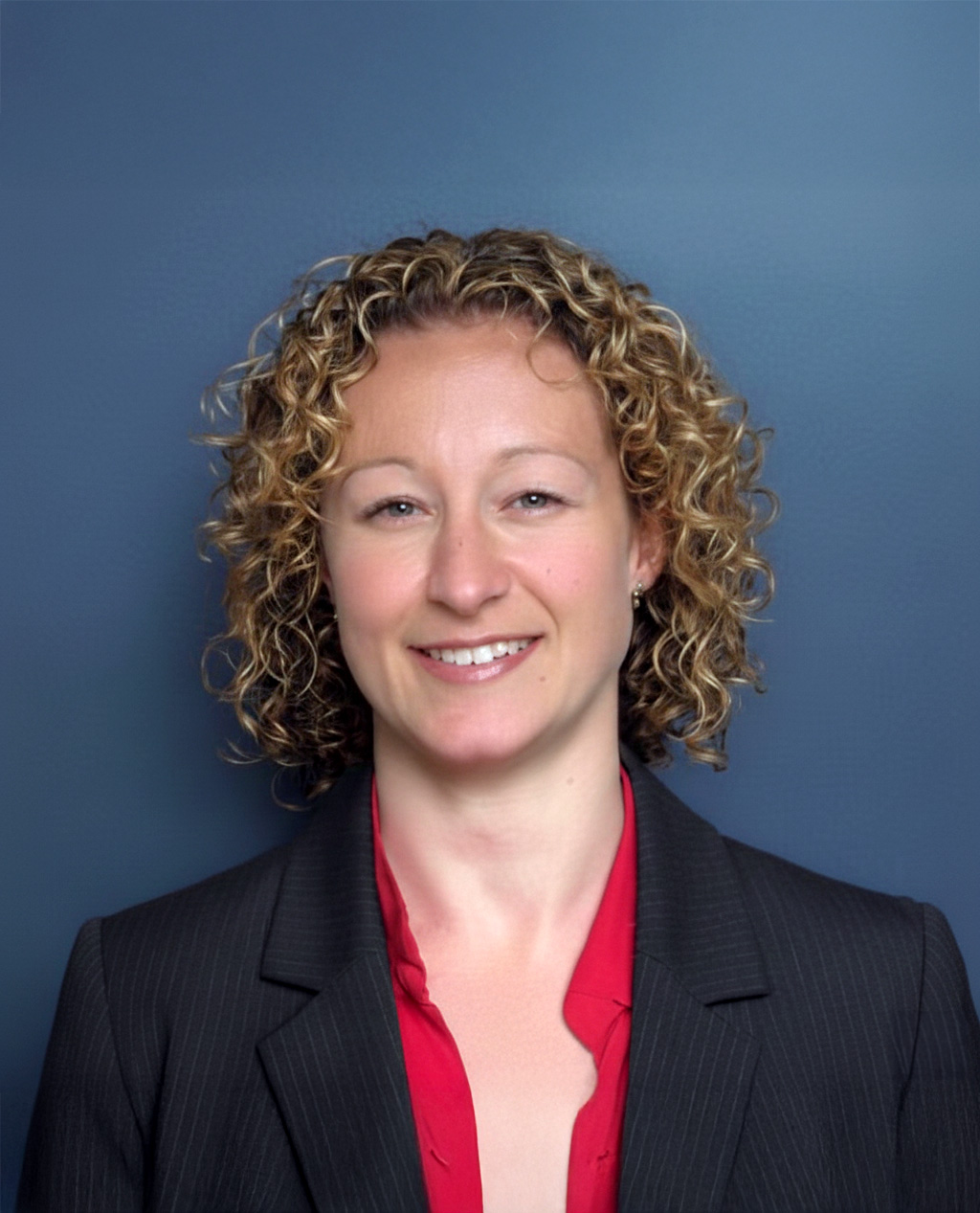 Portrait of Stacey Quinn, FCA, wearing a black pinstripe blazer and red blouse against a blue background.