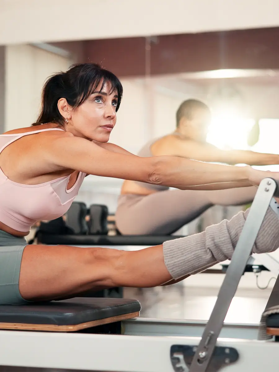 Woman in athletic wear stretching her leg forward on a Pilates reformer machine in a fitness studio.