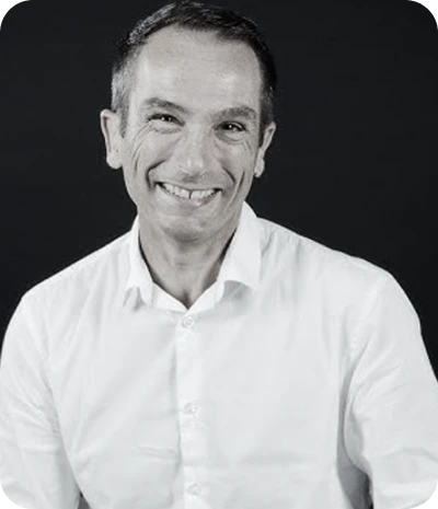 Portrait en noir et blanc d'un homme souriant portant une chemise blanche sur un fond sombre.