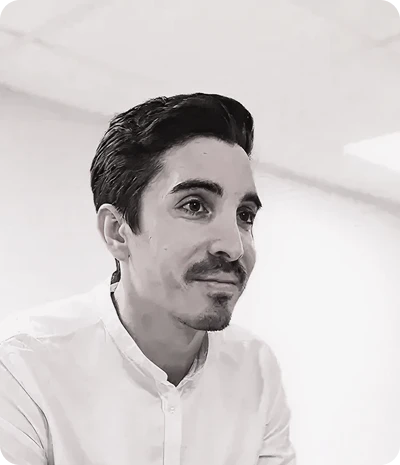 Portrait en noir et blanc d'un homme souriant portant une chemise blanche dans un intérieur clair.