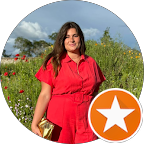 Femme en combinaison rouge debout dans un champ avec des fleurs et un ciel bleu en arrière-plan.