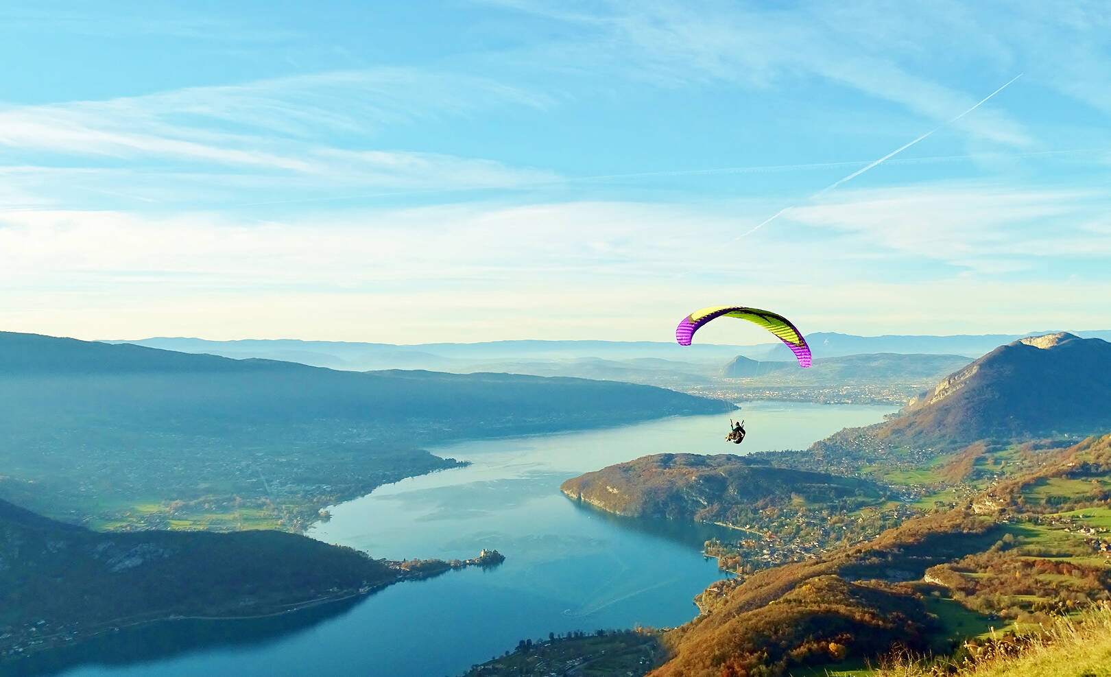 Un parapentiste vole au-dessus d'un lac entouré de montagnes sous un ciel bleu clair.