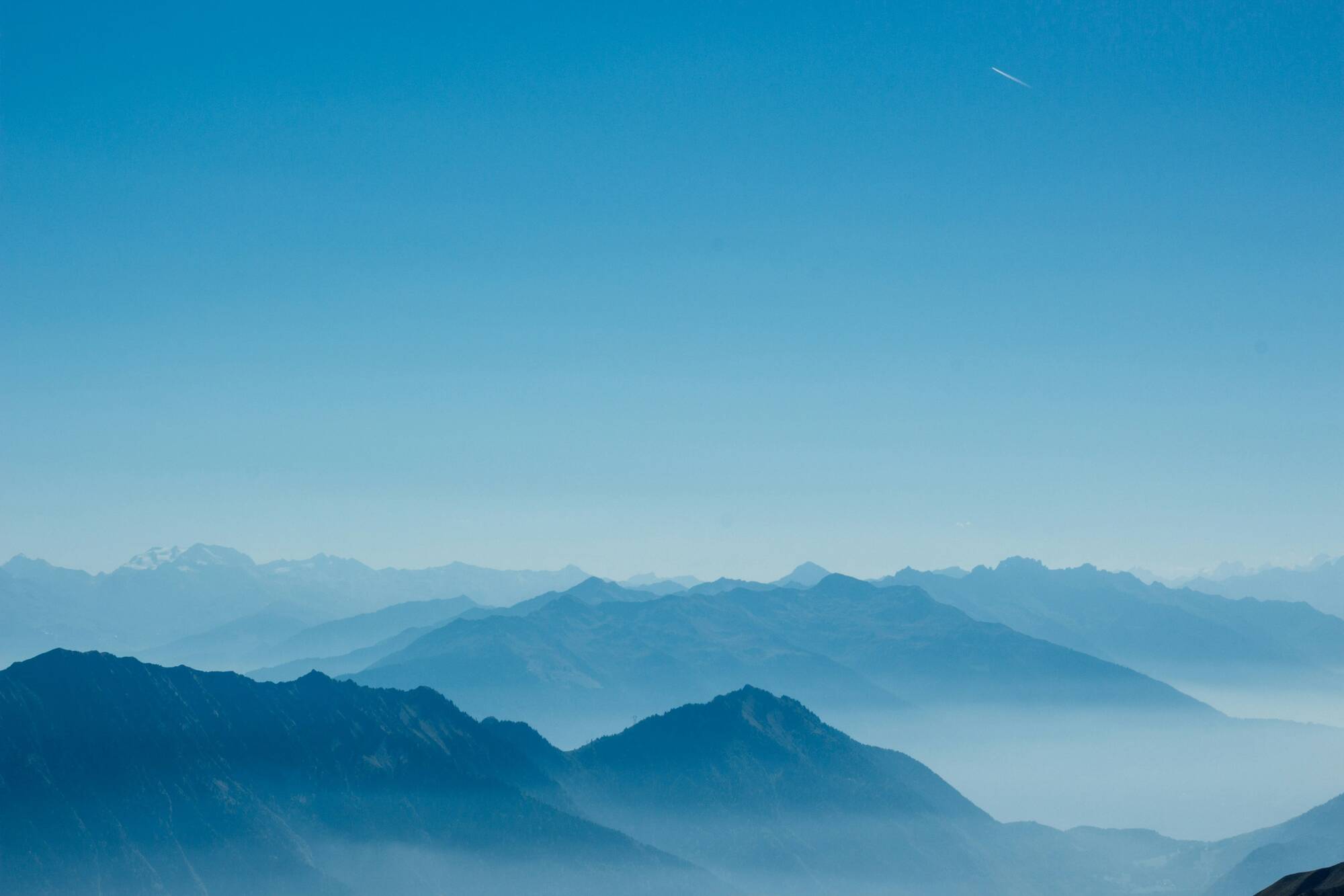 Chaîne de montagnes bleutées avec brume et ciel clair au-dessus.