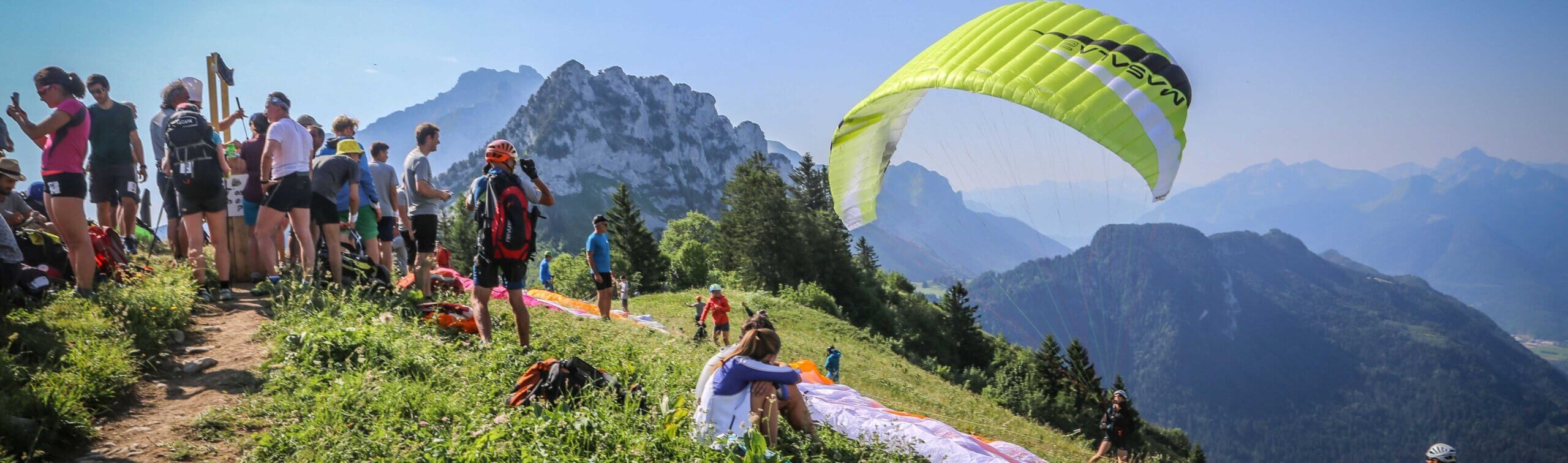 Gens attendant et préparant le parapente dans un paysage de montagnes ensoleillé.