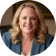 Smiling woman with shoulder-length blonde hair wearing a blue blazer in an indoor setting.