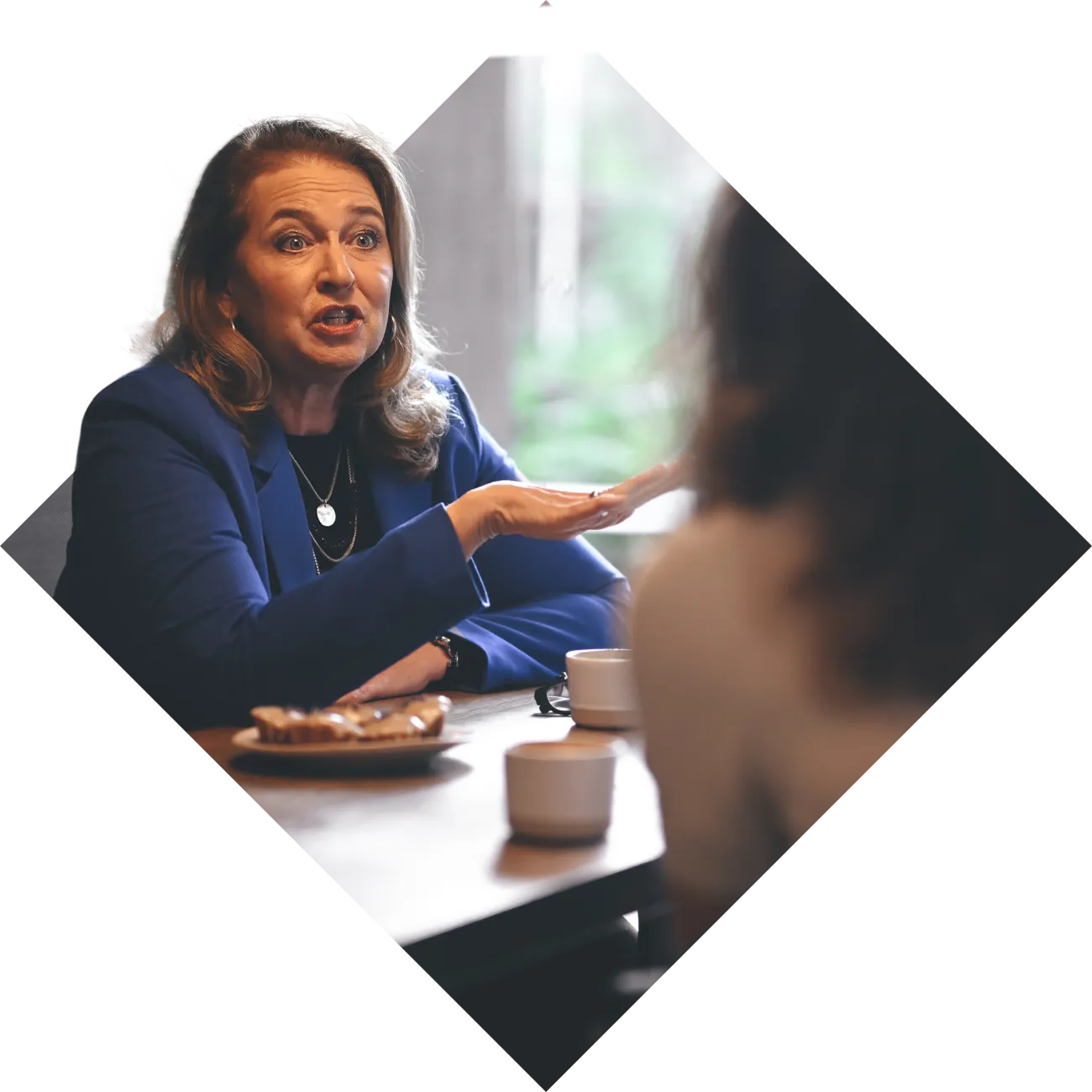 Professional woman gesturing while speaking during a meeting over coffee.