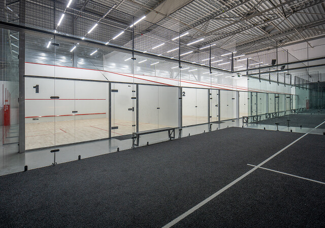 Indoor squash courts with glass walls numbered 1 and 2 under ceiling lights.