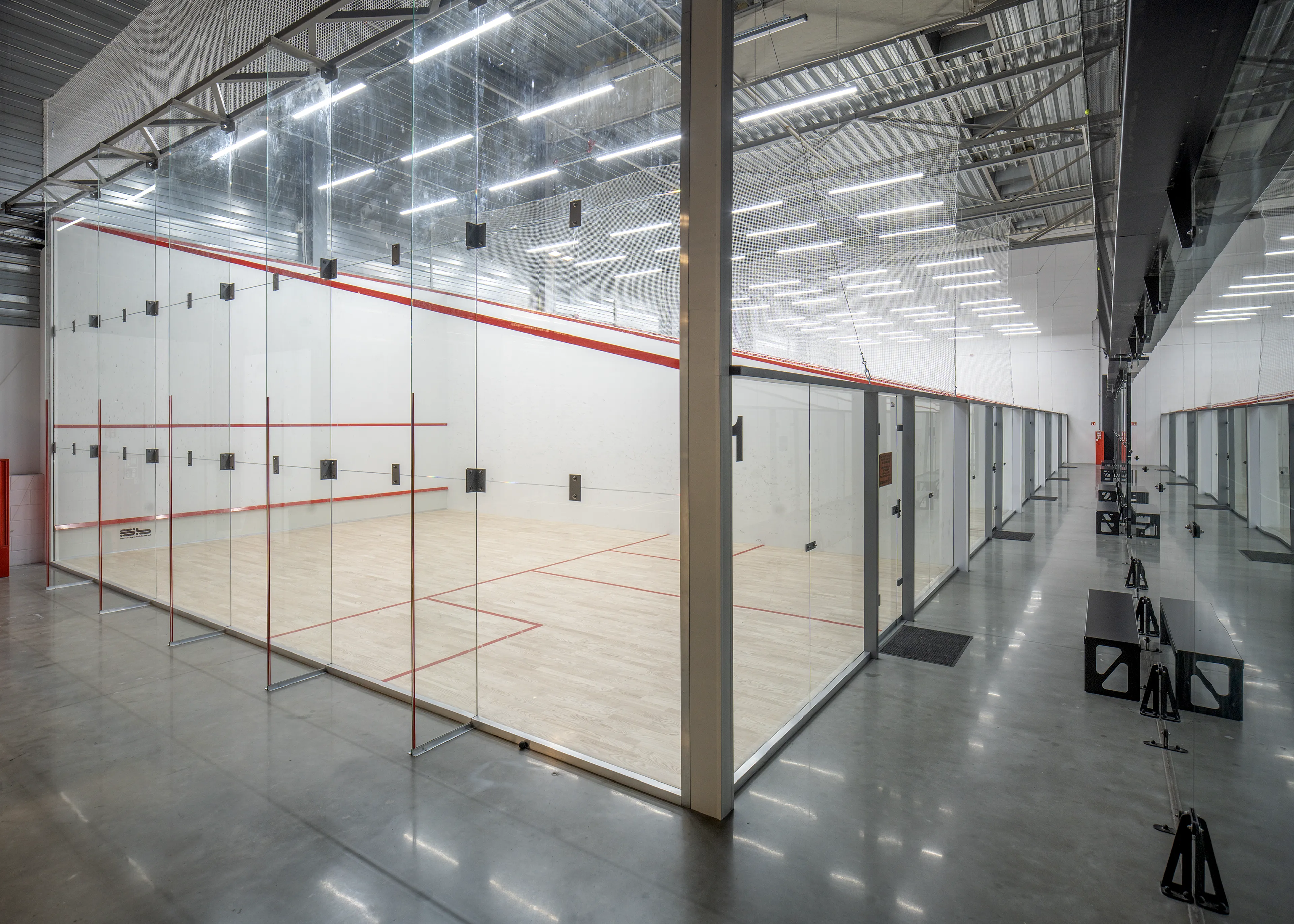 Indoor squash courts with glass walls and polished concrete floor in a well-lit sports facility.