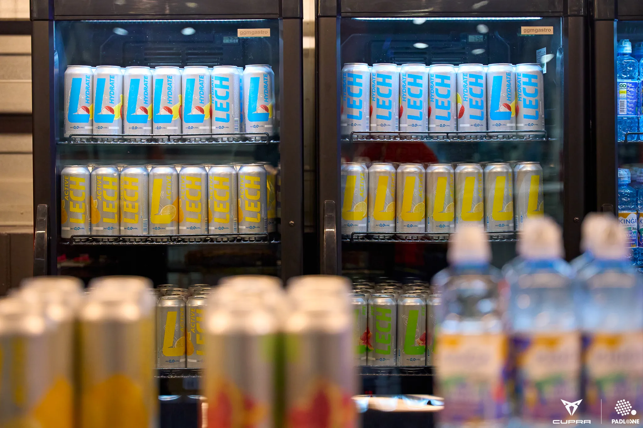 Refrigerated display with multiple rows of LECH Active non-alcoholic drink cans in different flavors and bottled water in the foreground.