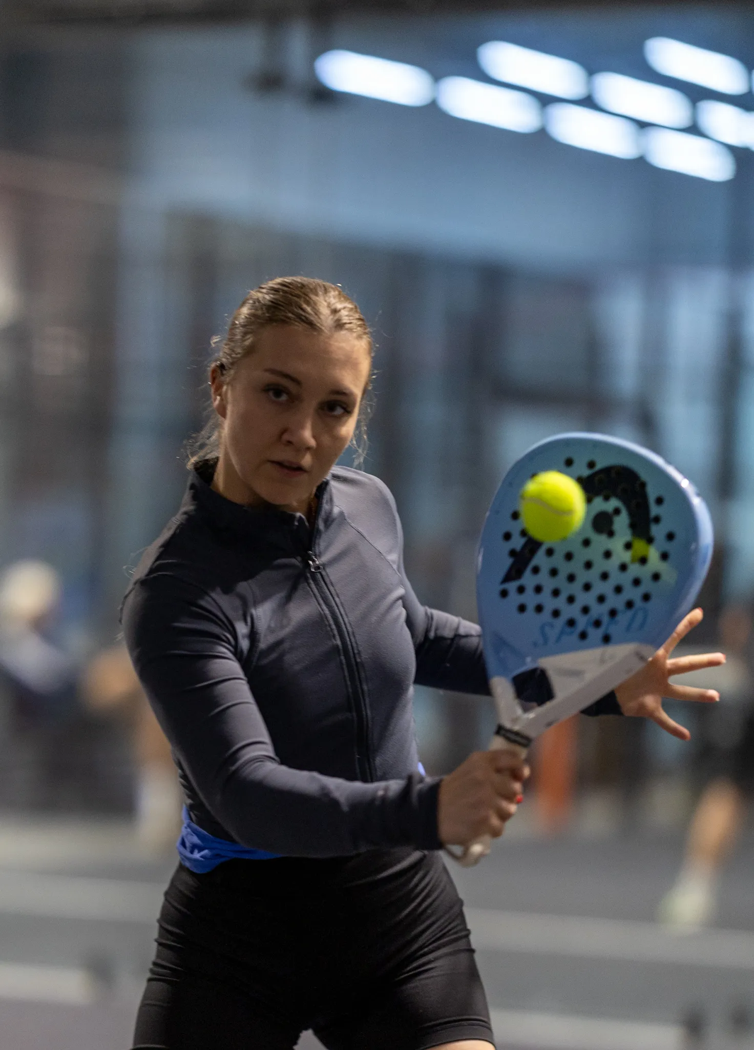 Young woman focused on hitting a yellow padel ball with a blue padel racket during a game.