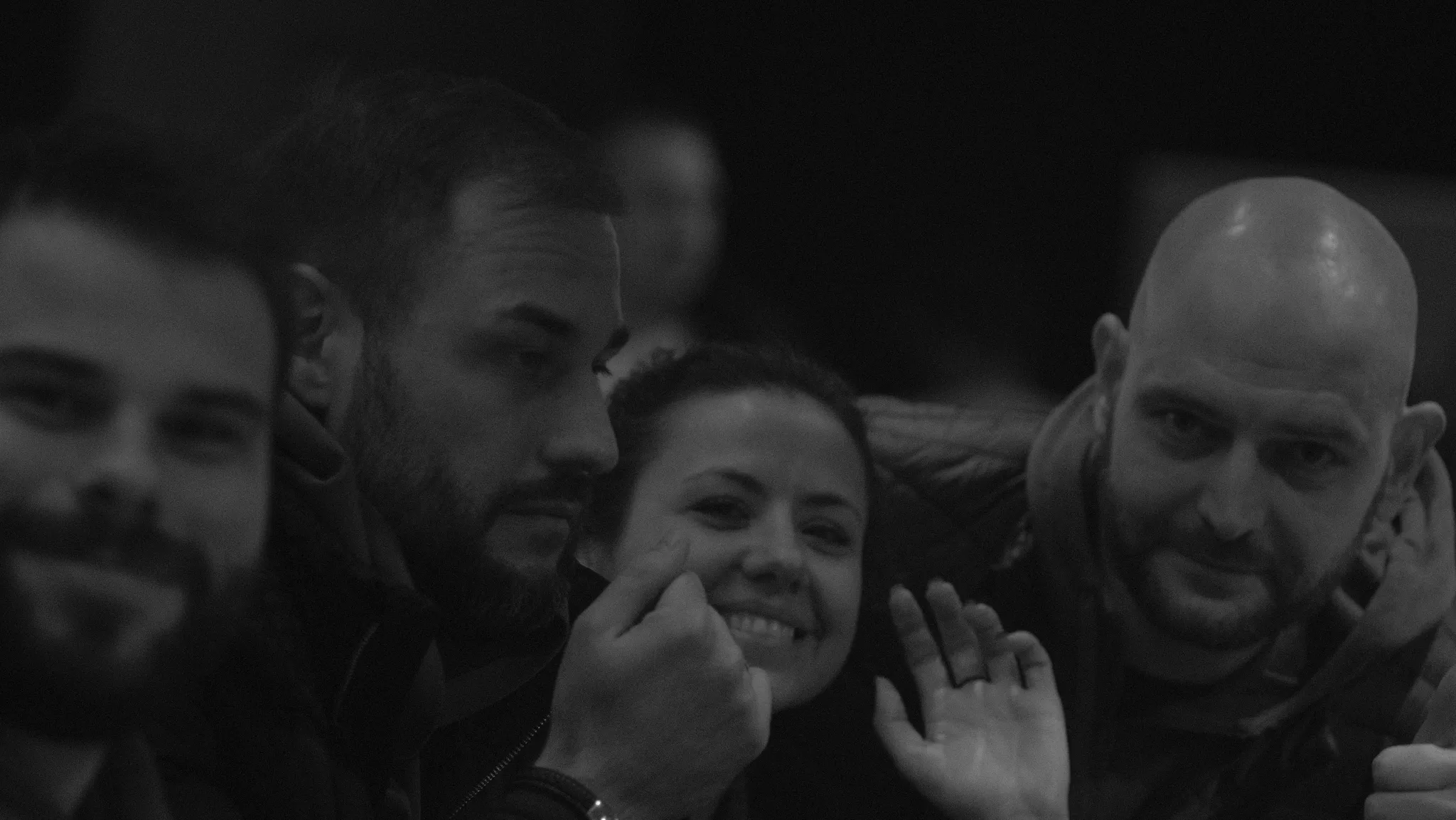 Black and white photo of four people closely gathered, with one woman smiling and waving at the camera.