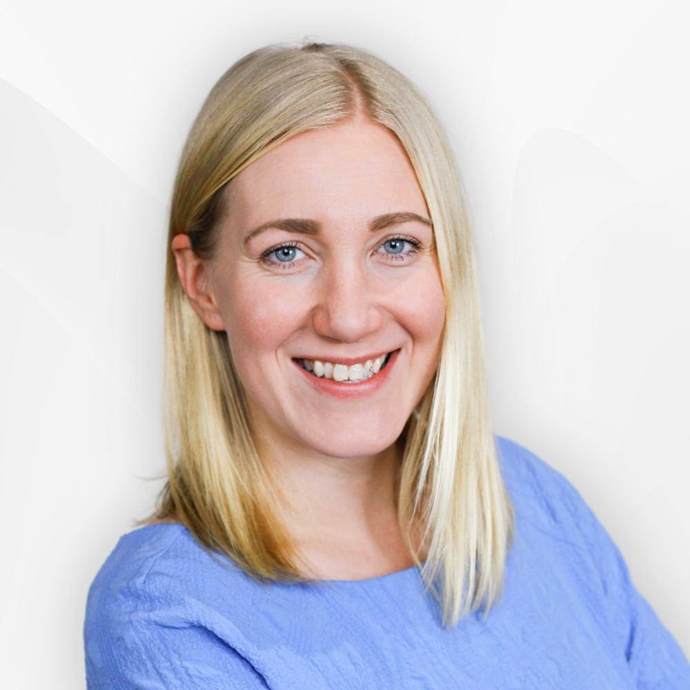 Smiling woman with straight blonde hair wearing a light blue textured top against a white background.