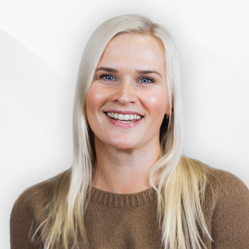 Smiling woman with long blonde hair wearing a brown sweater against a light background.