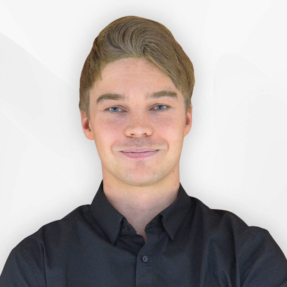 Portrait of a young man with light brown hair and blue eyes wearing a black button-up shirt, smiling slightly against a light background.