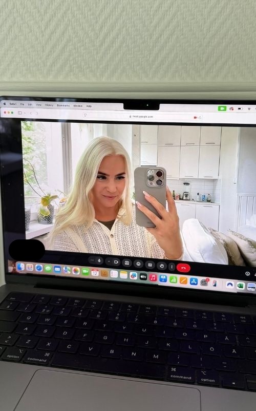 Person with long blond hair takes a selfie on a video call in a bright kitchen setting.