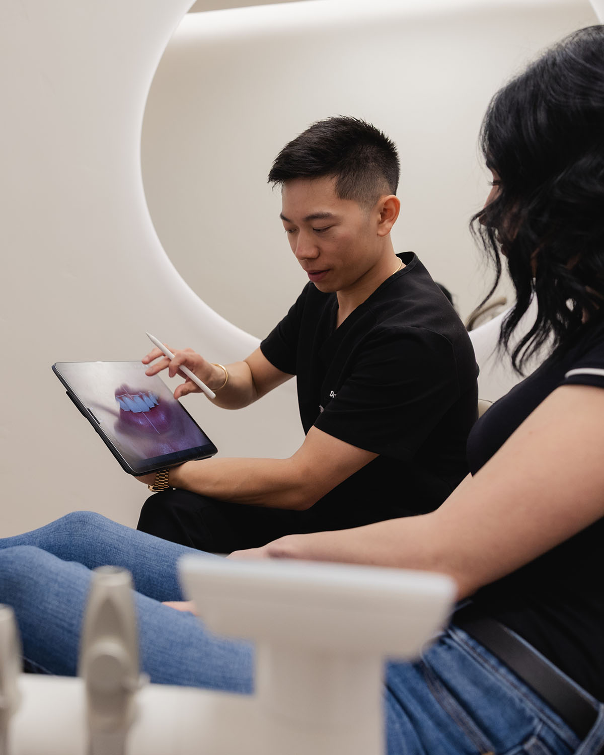 Dentist explains dental image on tablet to seated female patient in exam room.