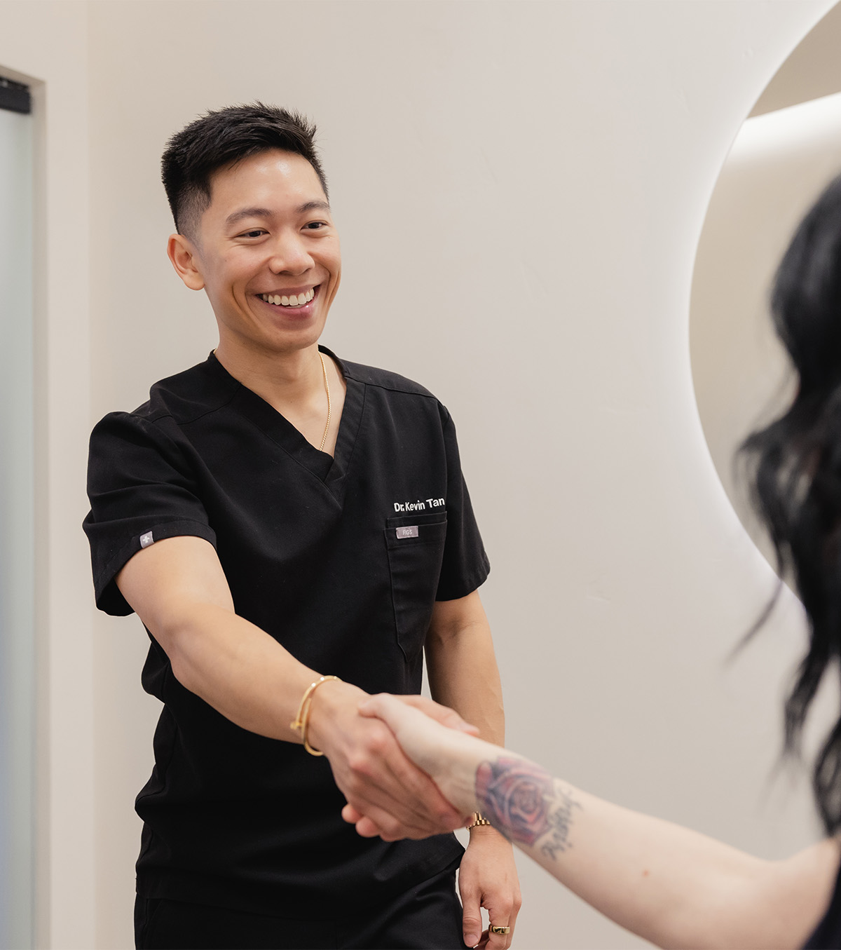 Smiling man in black scrubs shaking hands with a tattooed arm of another person.