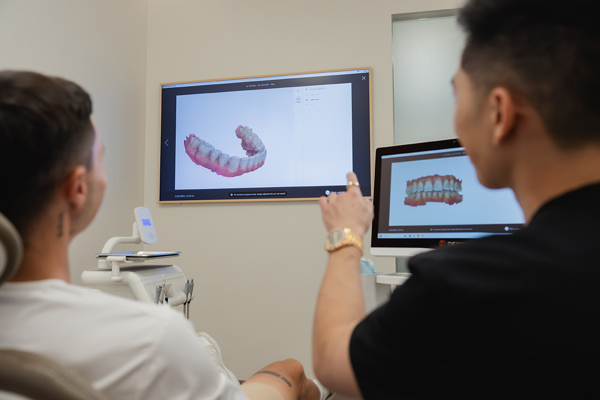 Dentist showing a 3D digital model of teeth on computer and wall screen to patient in dental clinic.