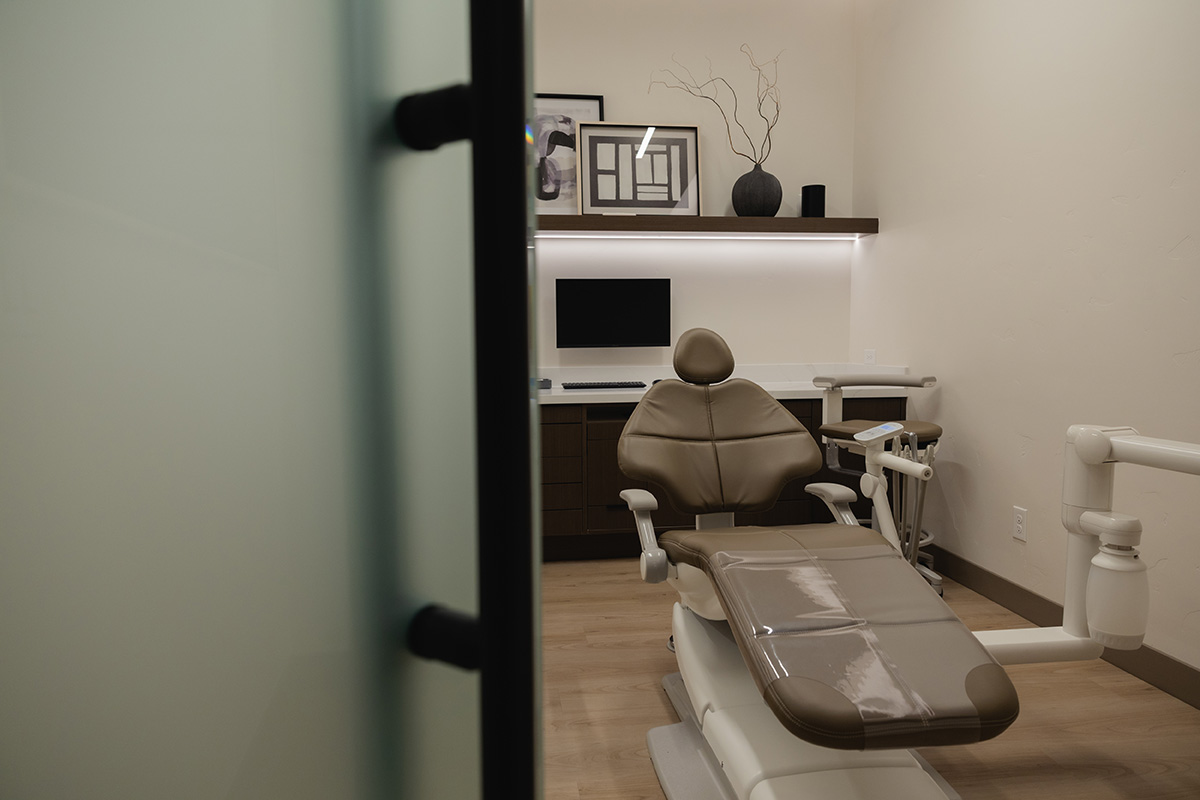 Modern dental examination room with brown dental chair, computer, and decorative shelf.