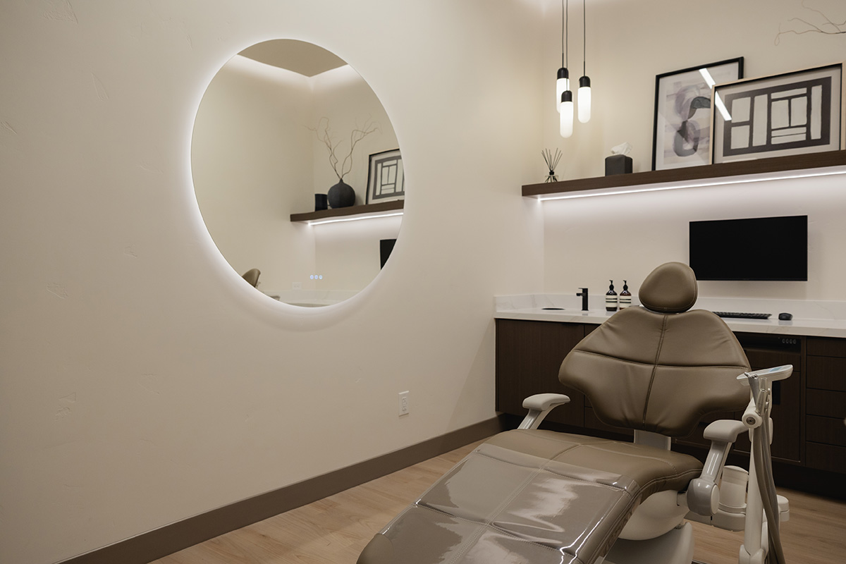 Modern dental office with brown exam chair, round mirror, and computer on counter.