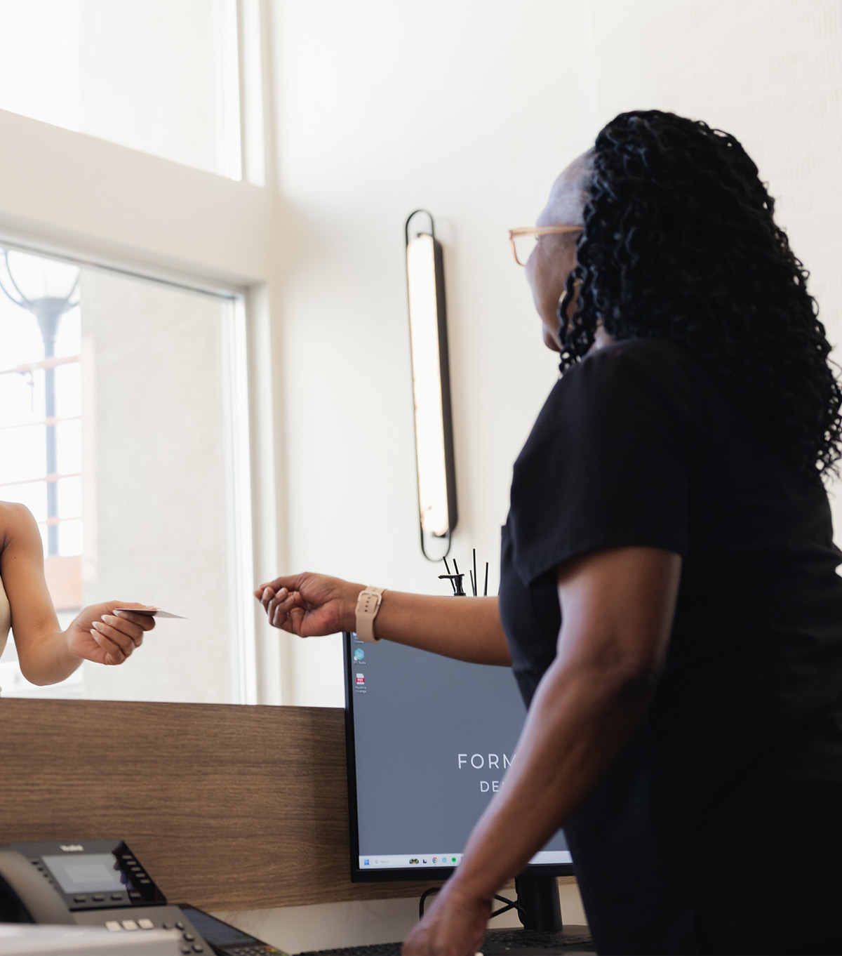Receptionist in black shirt reaching to take a card from a customer across the desk.