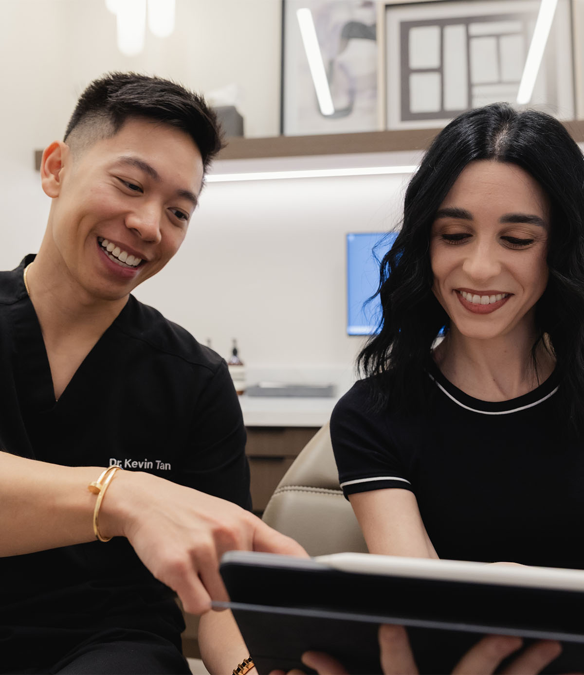 Smiling male healthcare professional shows a tablet to a female patient in a medical office.