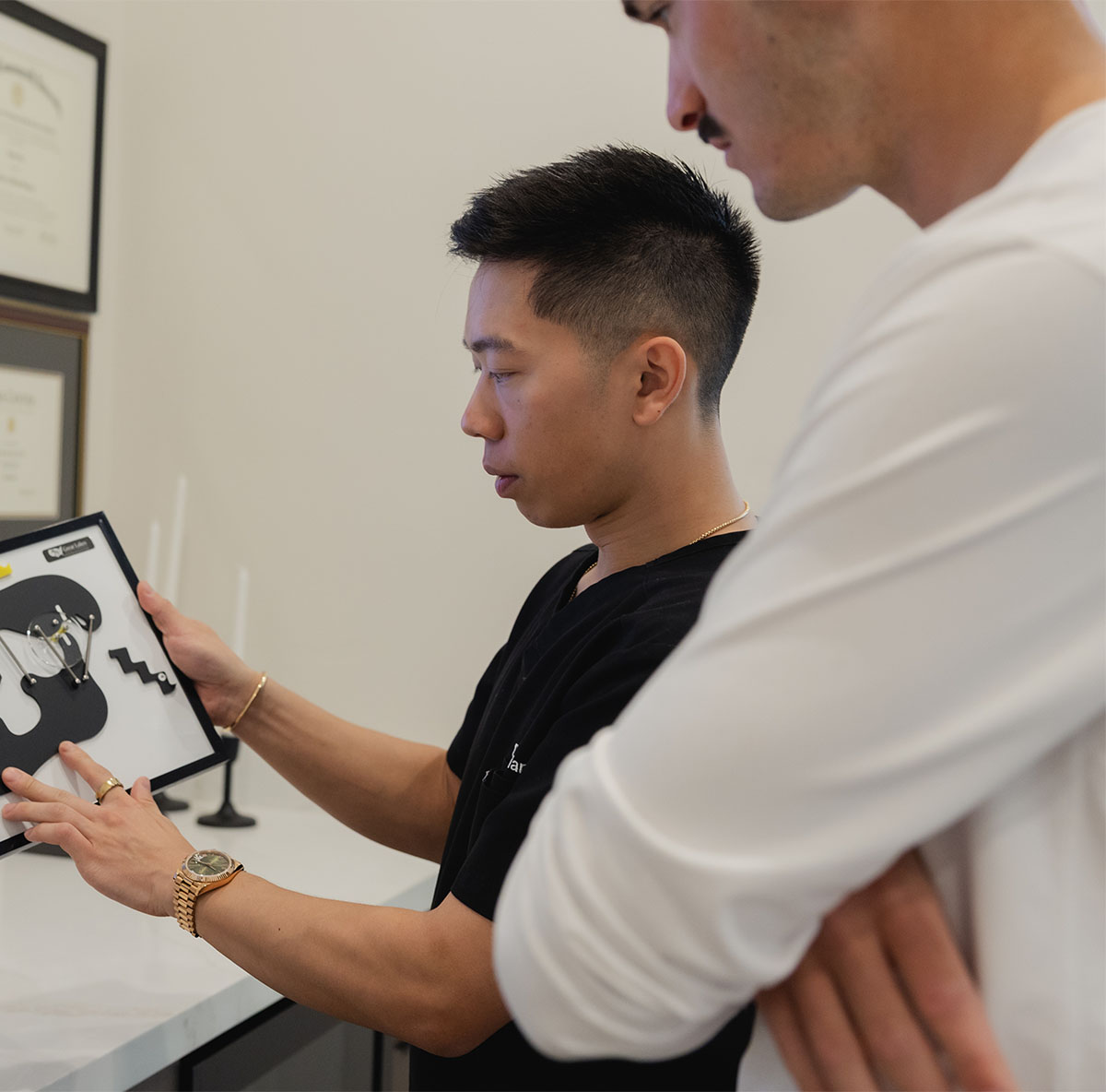 Man in black scrubs explaining ear anatomy model to another person in white top.