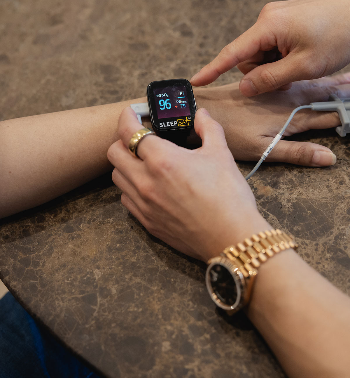 Person wearing a watch checking blood oxygen and heart rate on a SleepSat device on their wrist.