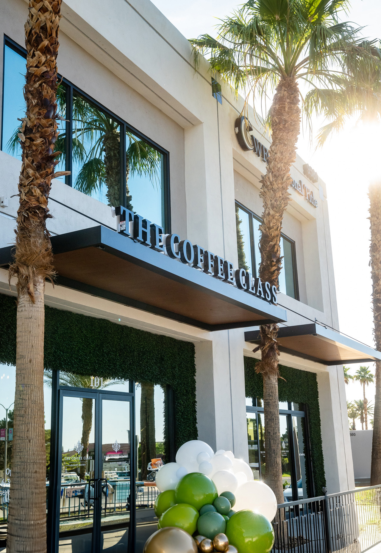 Exterior of The Coffee Class with palm trees and green, white, and gold balloons outside.