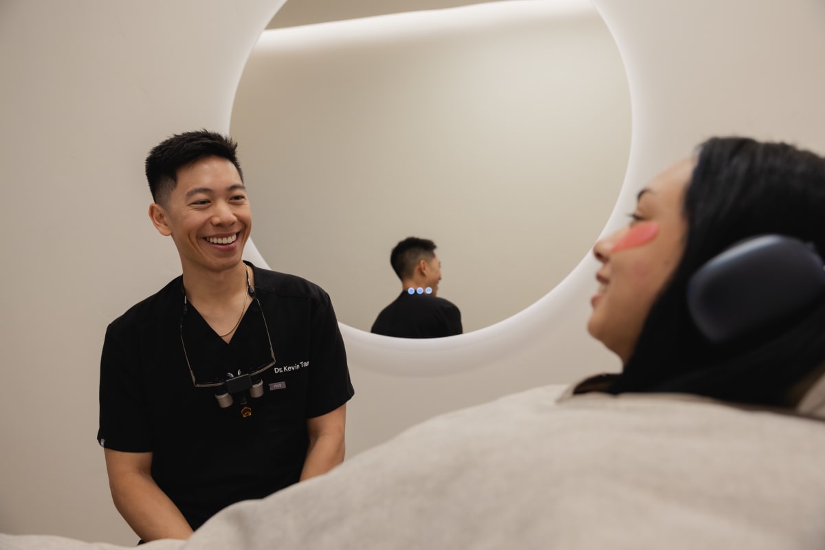 Dentist in black scrubs smiling at patient reclined in dental chair during examination