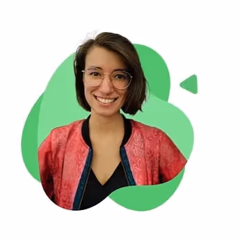 Junge Pädagogin mit kurzen braunen Haaren und Brille, die einen roten Cardigan über schwarzem Oberteil trägt und lächelt.