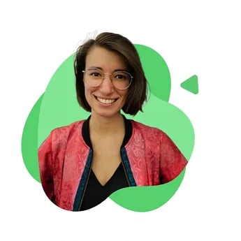 Junge Pädagogin mit kurzen braunen Haaren und Brille, die einen roten Cardigan über schwarzem Oberteil trägt und lächelt.