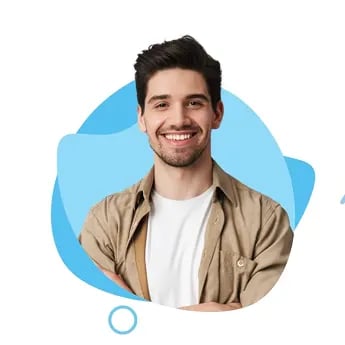 Ein lächelnder junger Lehrer mit dunklen Haaren trägt ein beiges Hemd über einem weißen T-Shirt vor blauem Hintergrund.