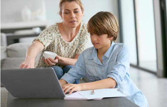 Mutter hilft ihrem Sohn bei den Hausaufgaben mit einem Laptop auf dem Tisch.