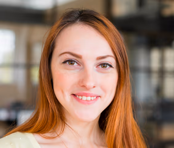 Porträt einer lächelnden jungen Frau mit langen roten Haaren in einem modernen Büro.