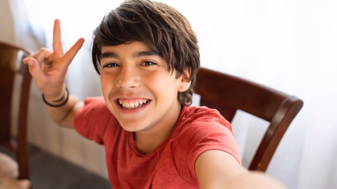 Lächelnder Schüler in rotem T-Shirt macht ein Friedenszeichen mit der Hand.