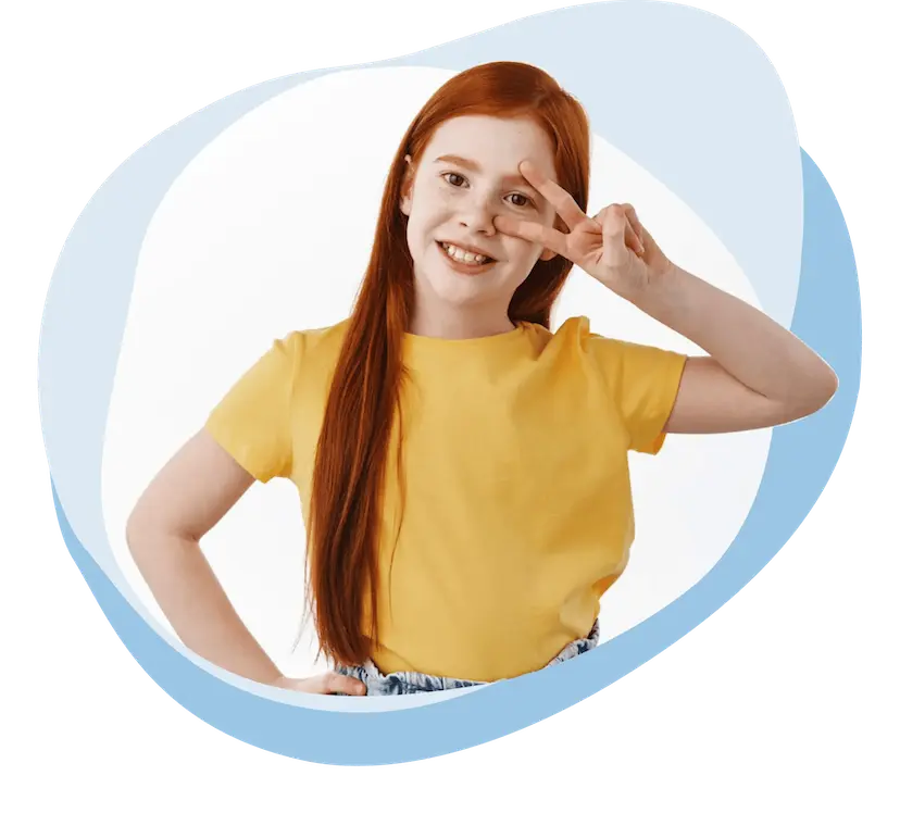 Lächendes rothaariges Mädchen in gelbem T-Shirt zeigt zwei Finger im V vor ihrem linken Auge.