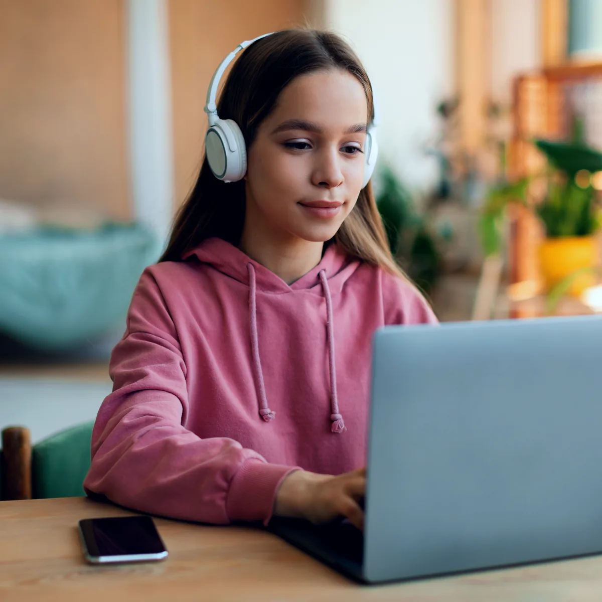 Mädchen im rosa Pullover schreibt neben ihrem Laptop