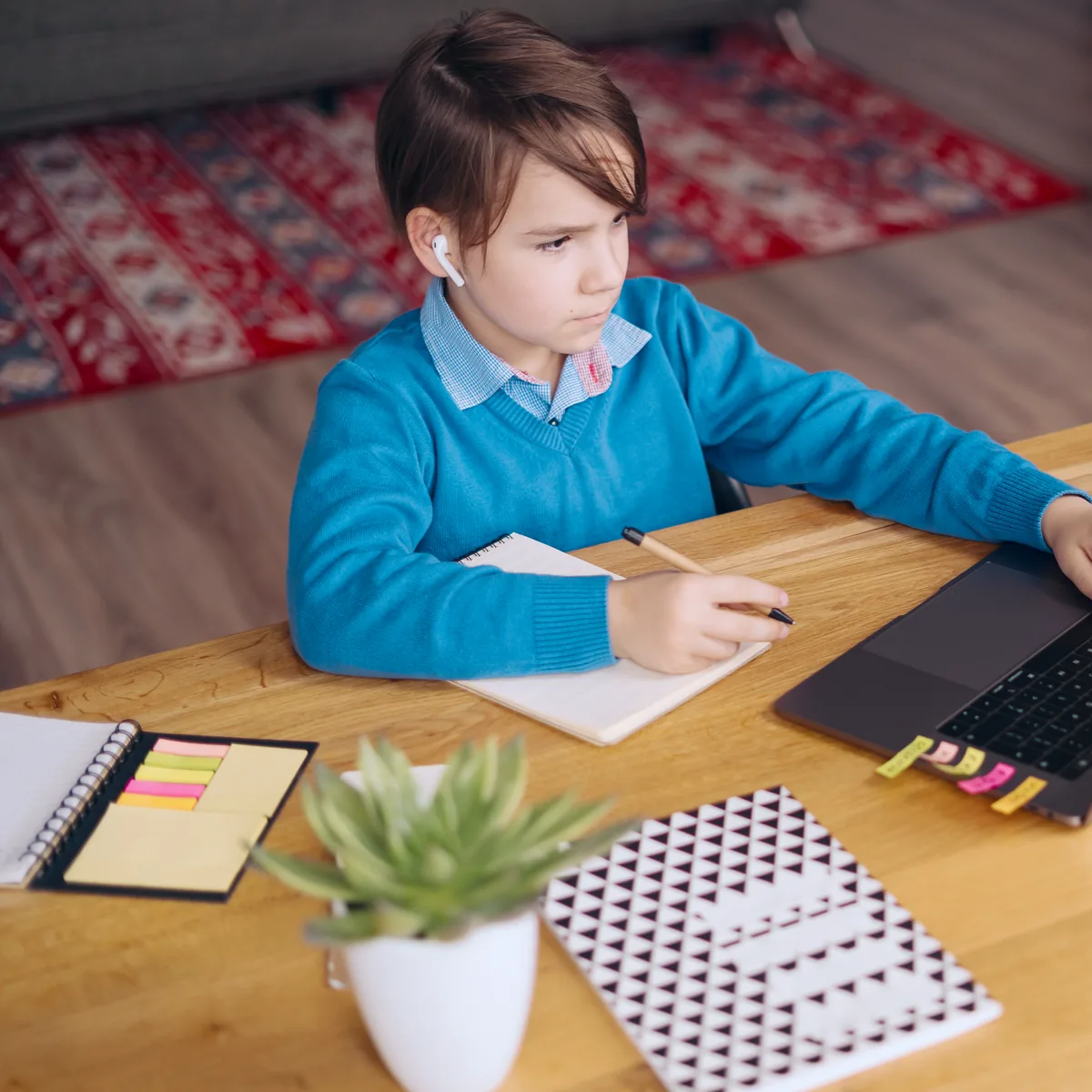 Junge im blauen Pullover arbeitet am Schreibtisch am Laptop