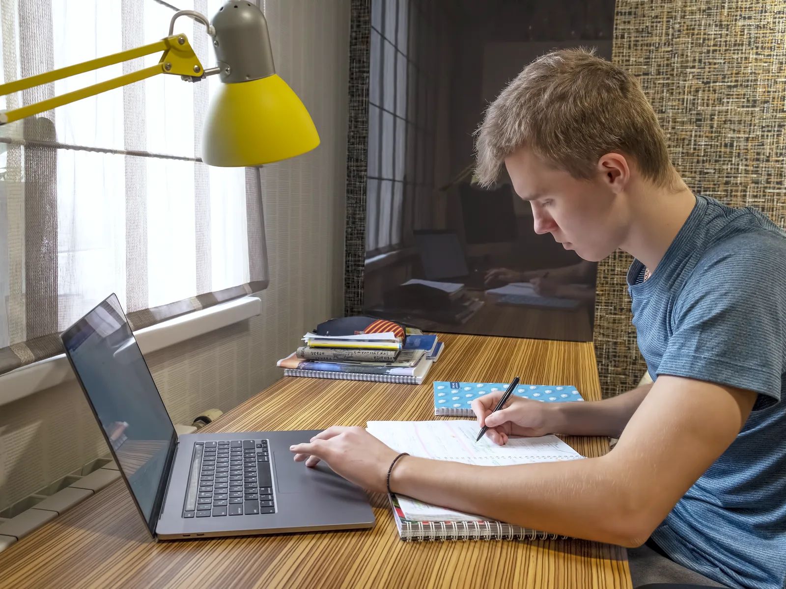Junge macht sich am Schreibtisch neben seinem Laptop Notizen
