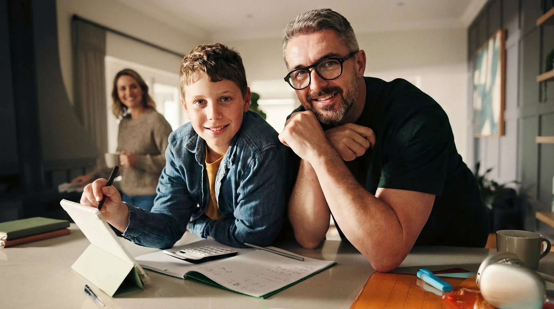 Vater und Sohn machen gemeinsam Hausaufgaben am Tablet, die Mutter im Hintergrund
