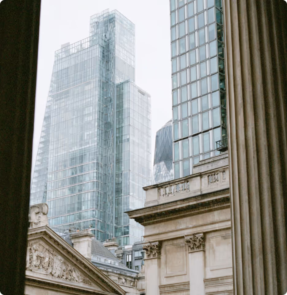 Modern glass skyscrapers rising behind classical stone buildings with ornate details and large columns.
