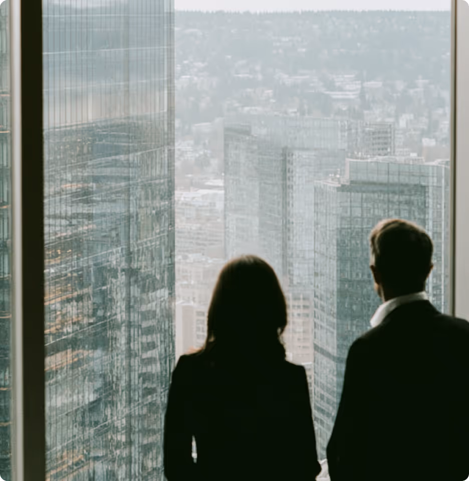 Silhouettes of a man and a woman in business attire looking out a large window at city skyscrapers.