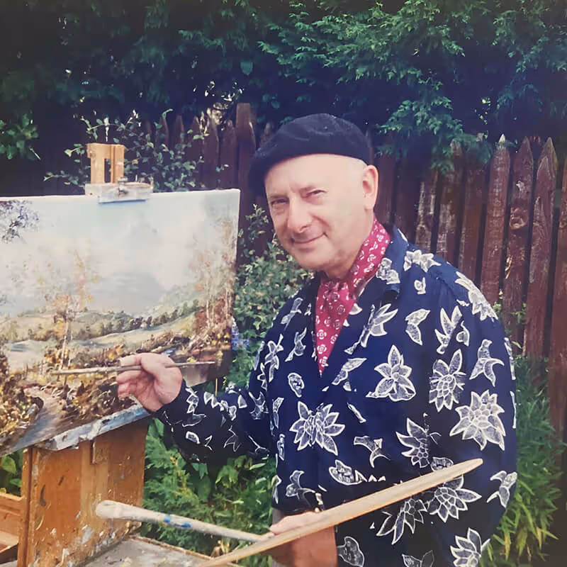 John Corcoran painting a landscape on an easel outdoors.