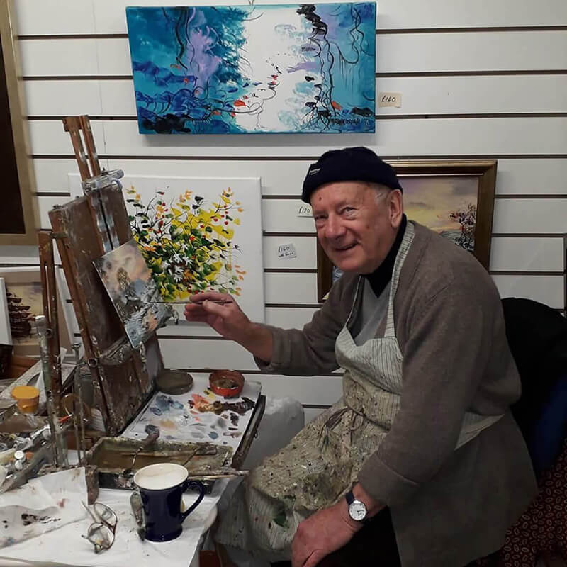 John Corcoran painting a landscape on a small canvas in an art studio.