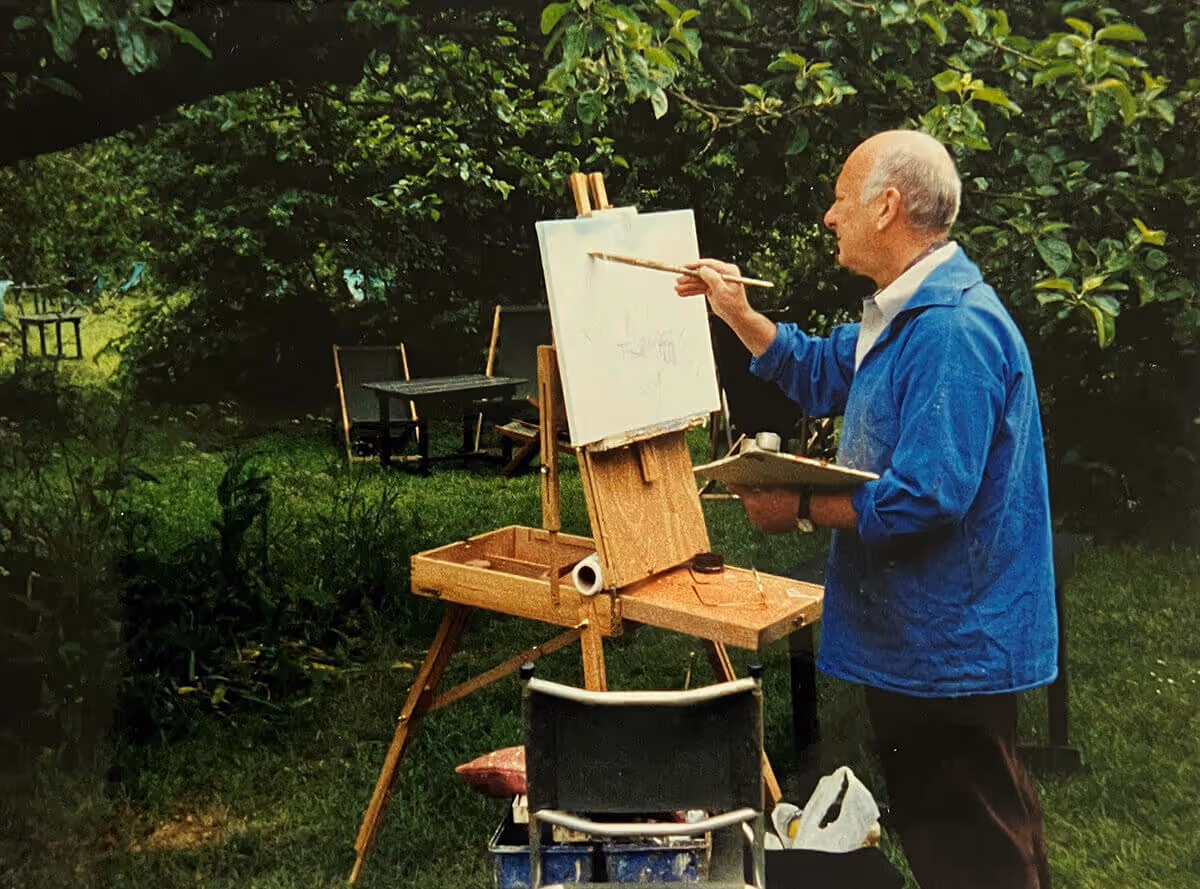 John Corcoran painting on a canvas set up on an easel in a vibrant green outdoor environment.