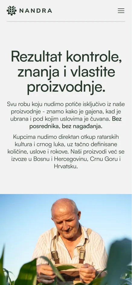 Smiling elderly man in overalls inspecting a plant leaf in a green field under blue sky.