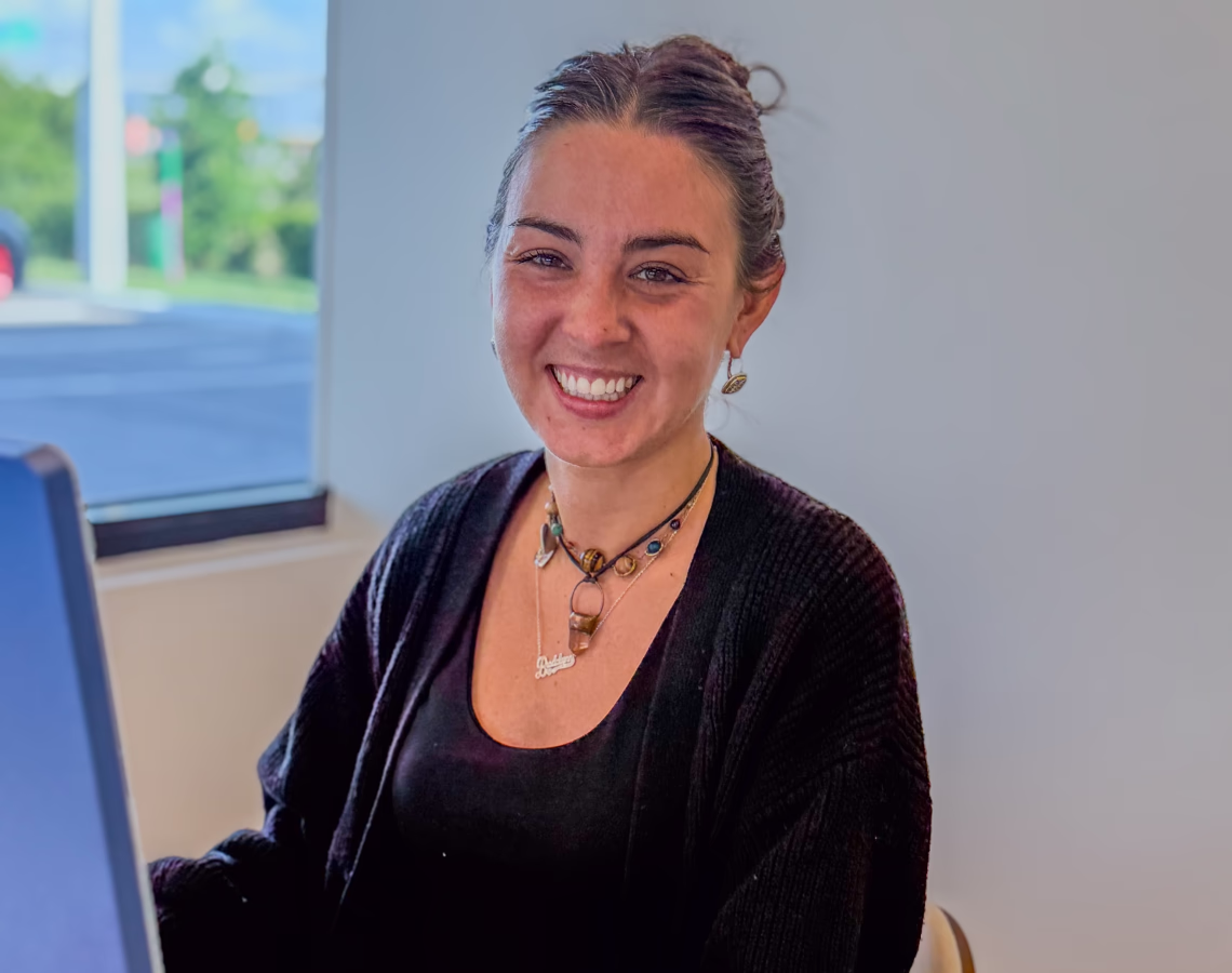 Smiling woman in a dental office wearing a black top, cardigan, and layered necklaces.