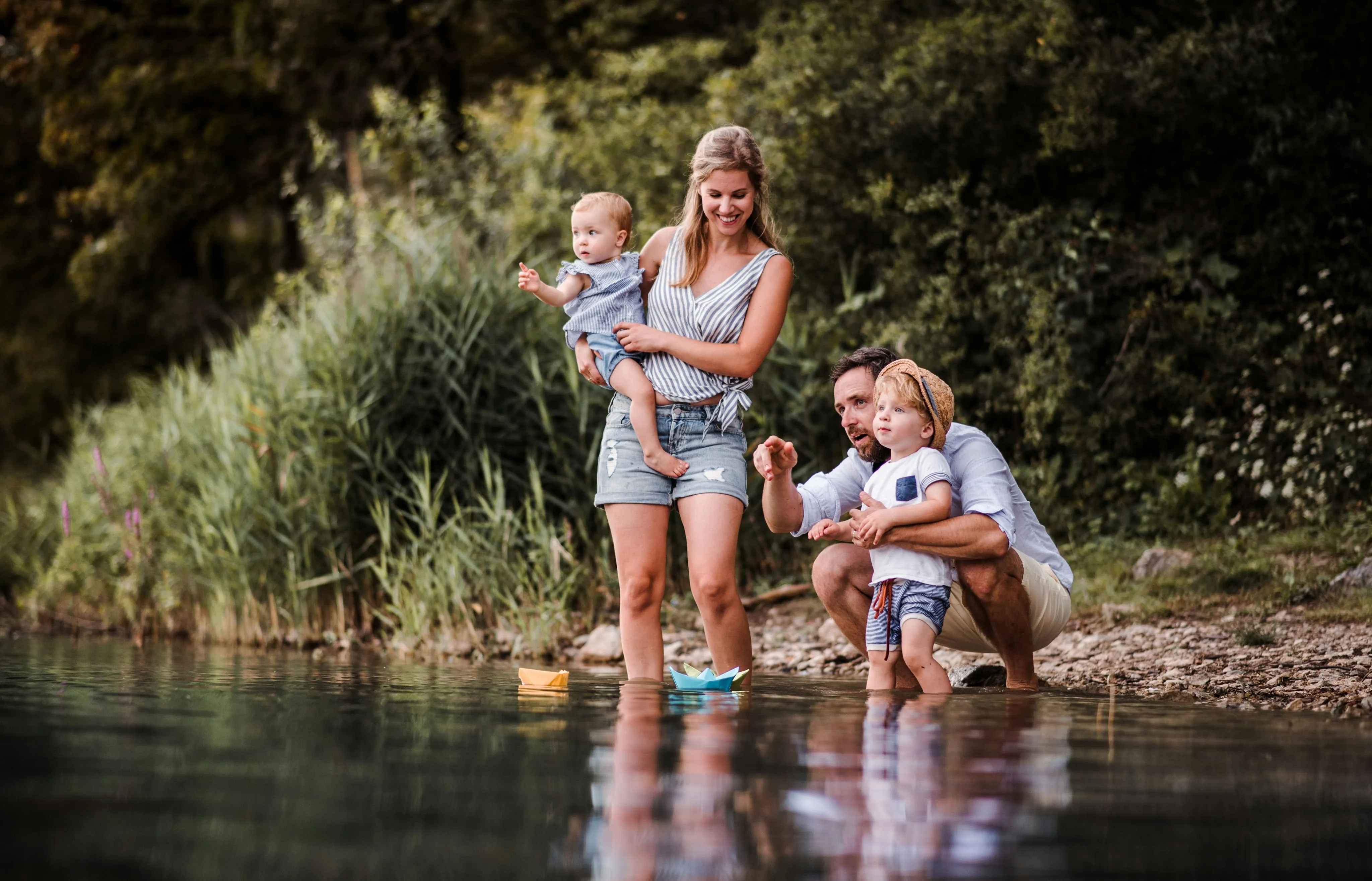 Family standing in a shallow mountain creek with young children playing along the shoreline