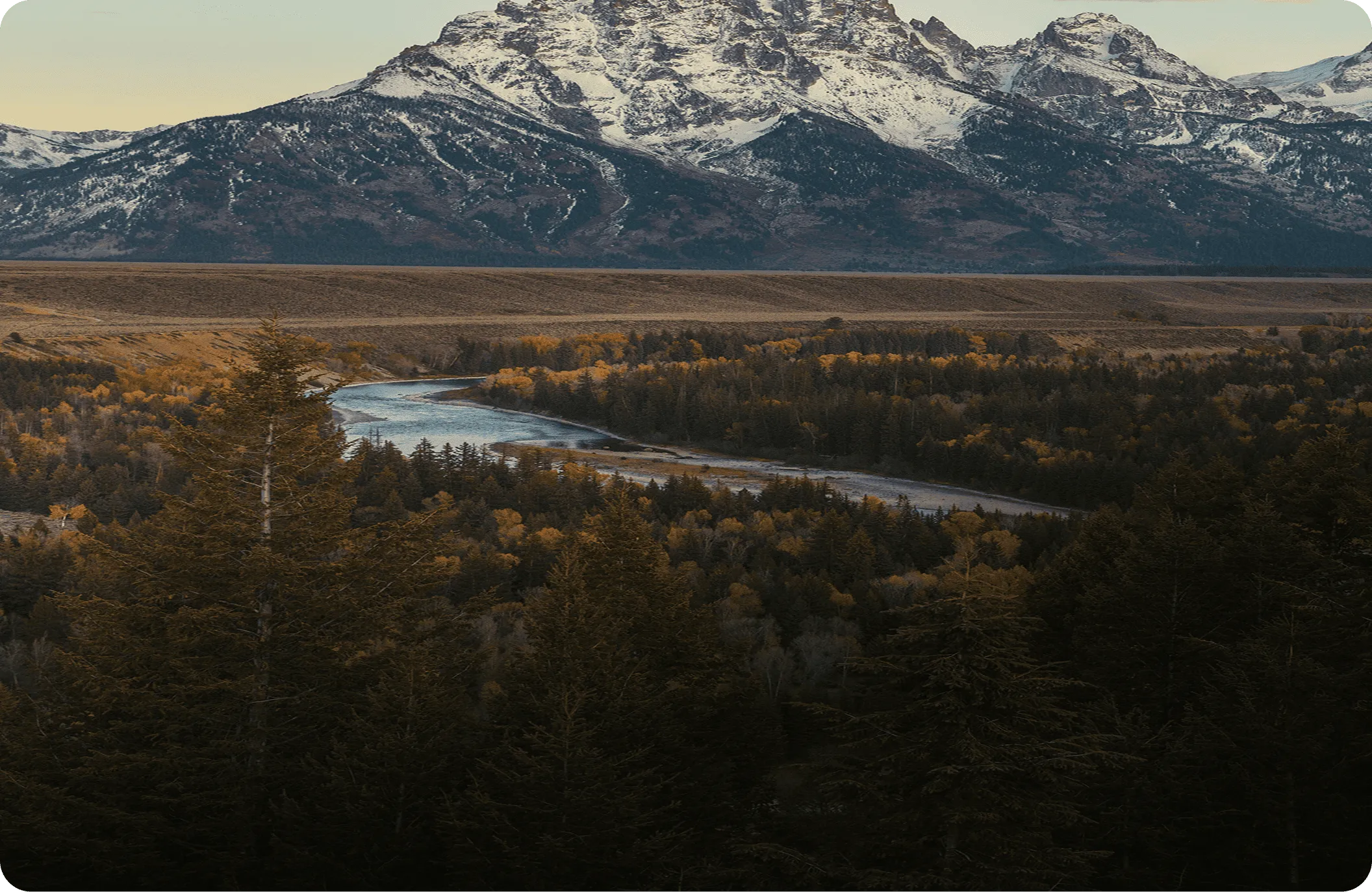 Wide mountain valley with a winding river and snow-capped peaks under a cloudy sky